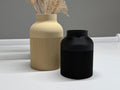 Two vases, one beige and one black, on a white surface with a gray background.