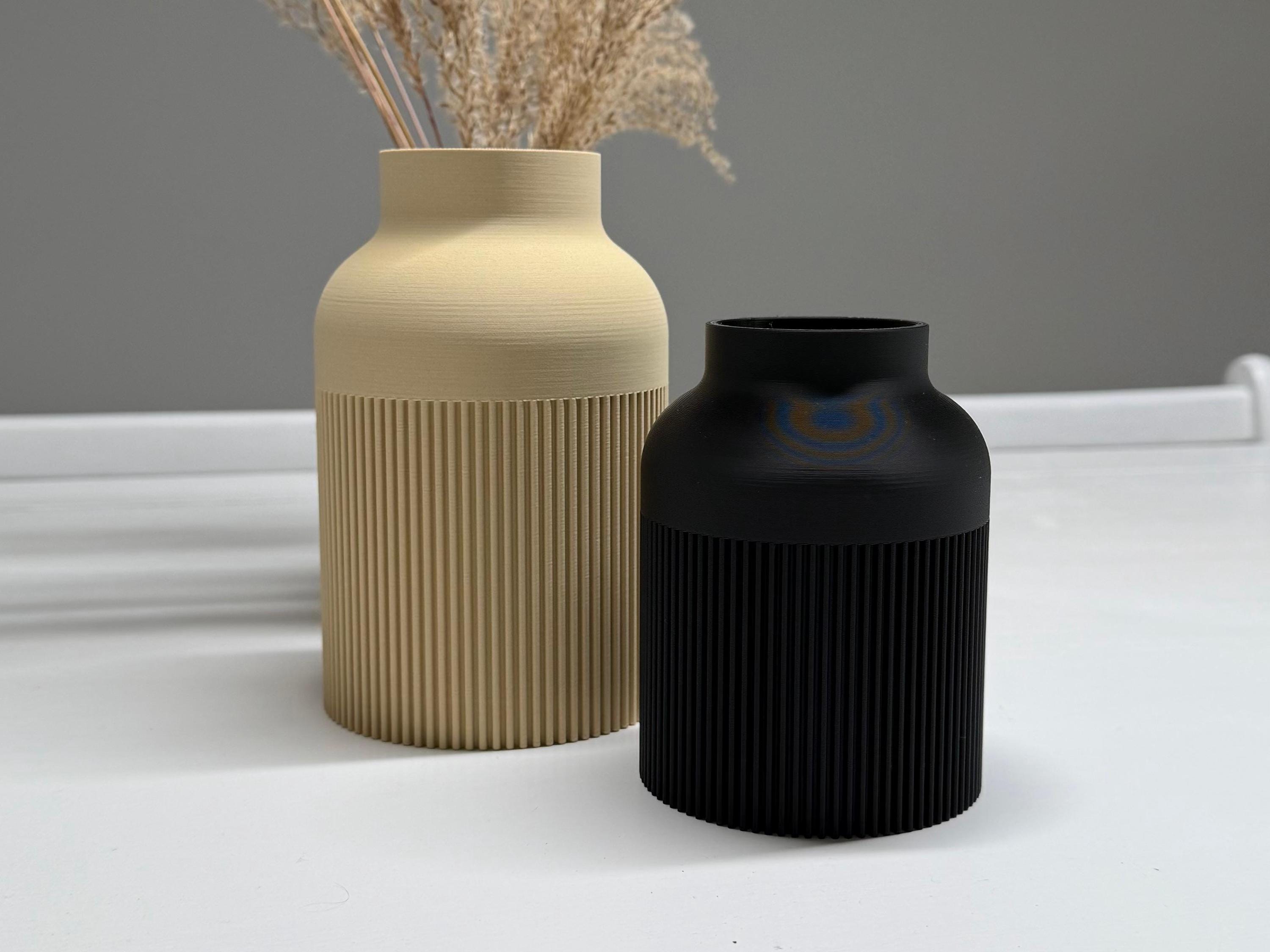 Two vases, one beige and one black, on a white surface with a gray background.