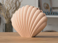 Shell-shaped decorative vase on a wooden surface with a blurred indoor background