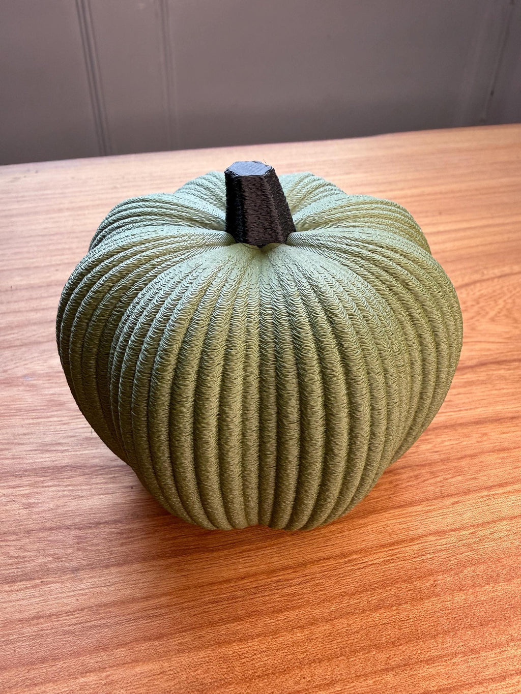Green textured pumpkin on a wooden surface with a neutral background