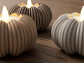 Ceramic pumpkin-shaped candles with lit wicks on a wooden surface