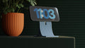 Digital clock with blue display showing time '11:03' next to a potted plant on a dark background