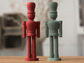 Two figurines, one red and one green, on a wooden surface with a blurred background.
