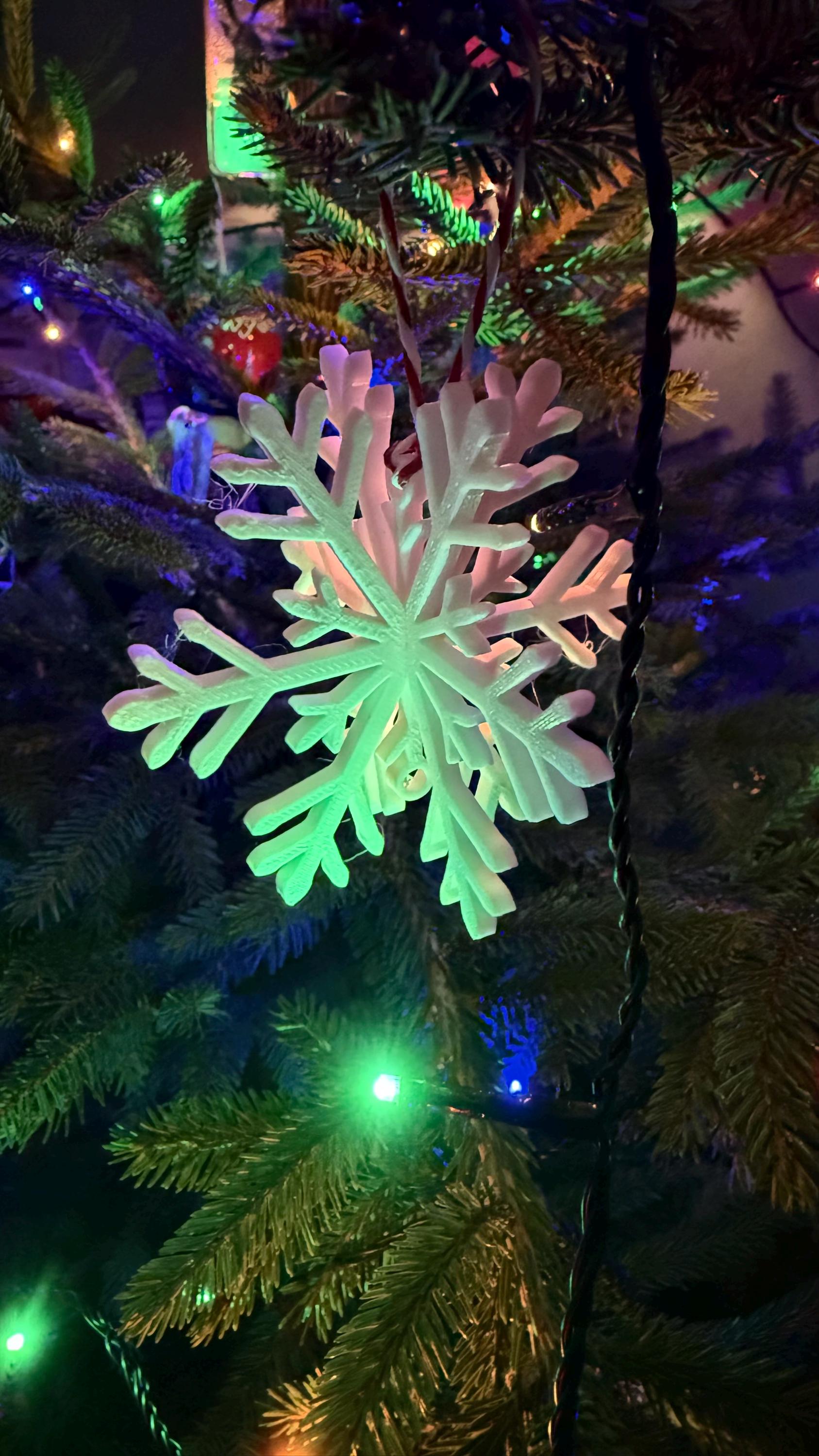 Glowing snowflake ornament on a Christmas tree with colorful lights.