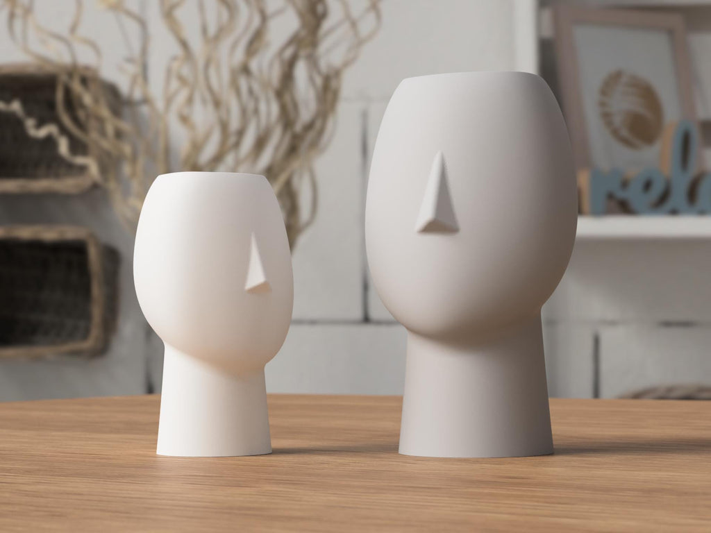 Two white ceramic face-shaped vases on a wooden surface with a blurred indoor background.