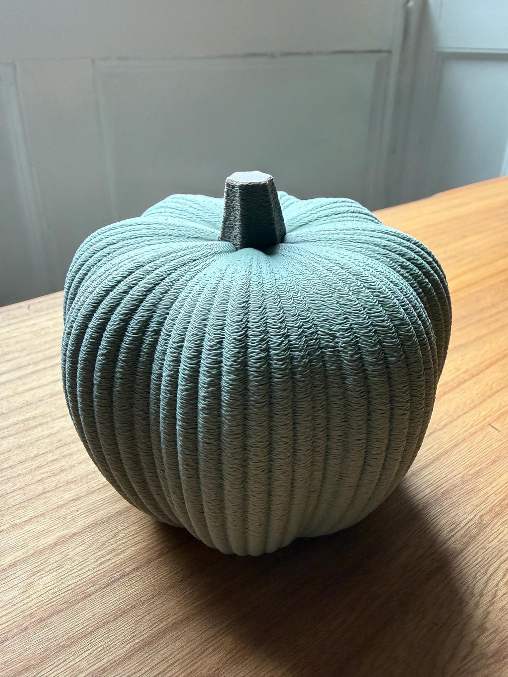 Teal textured pumpkin on a wooden surface with a white wall background