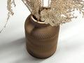 Cardboard vase with wavy pattern holding dried plants on a white background