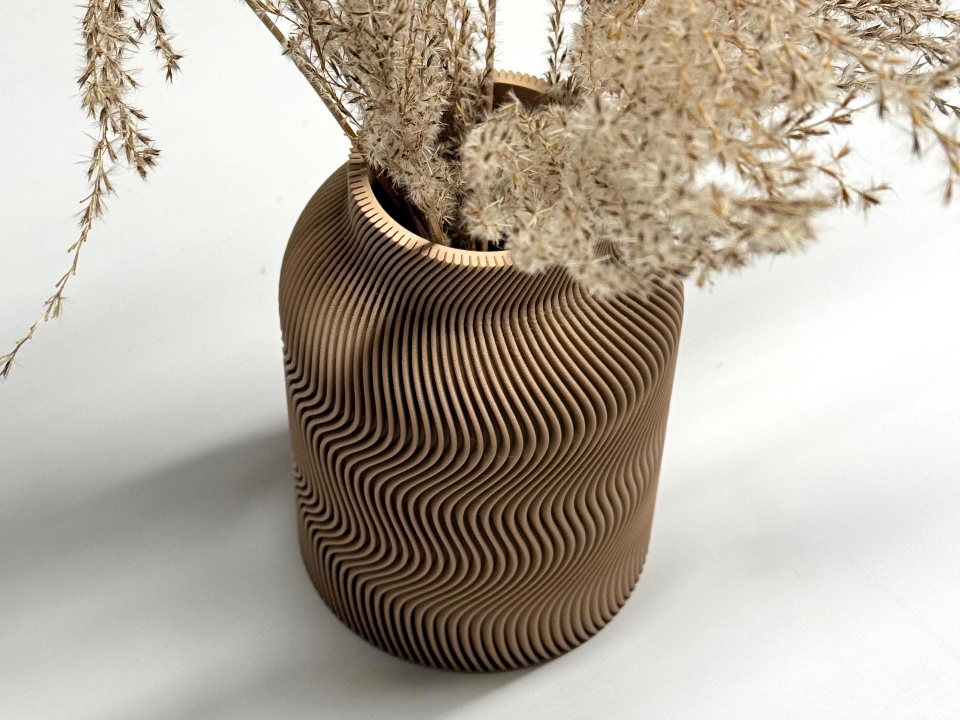 Cardboard vase with wavy pattern holding dried plants on a white background