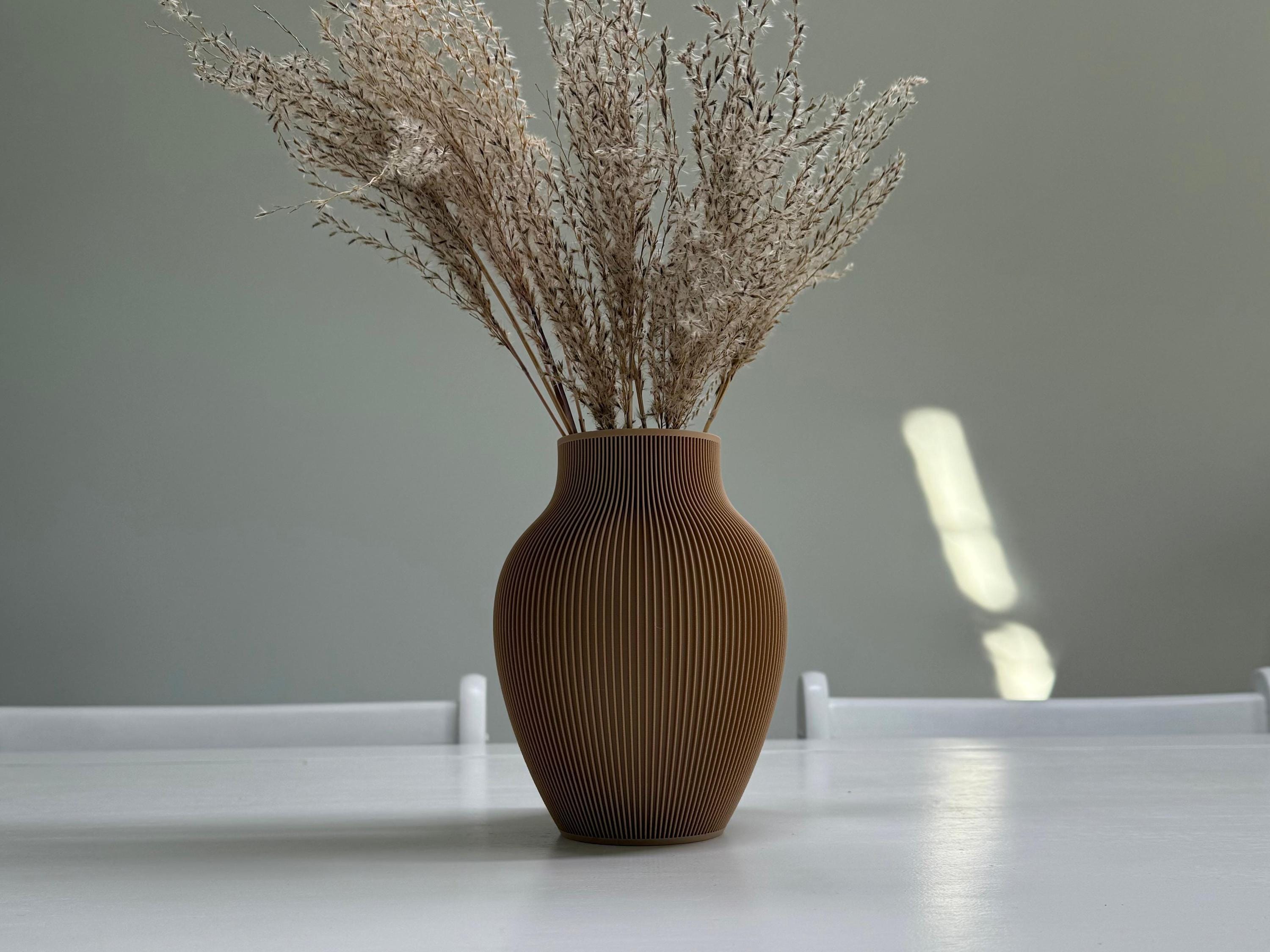 Brown textured vase with dried plants on a white surface against a gray background
