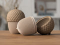 Three ceramic acorn-shaped containers on a wooden surface with a blurred indoor background.