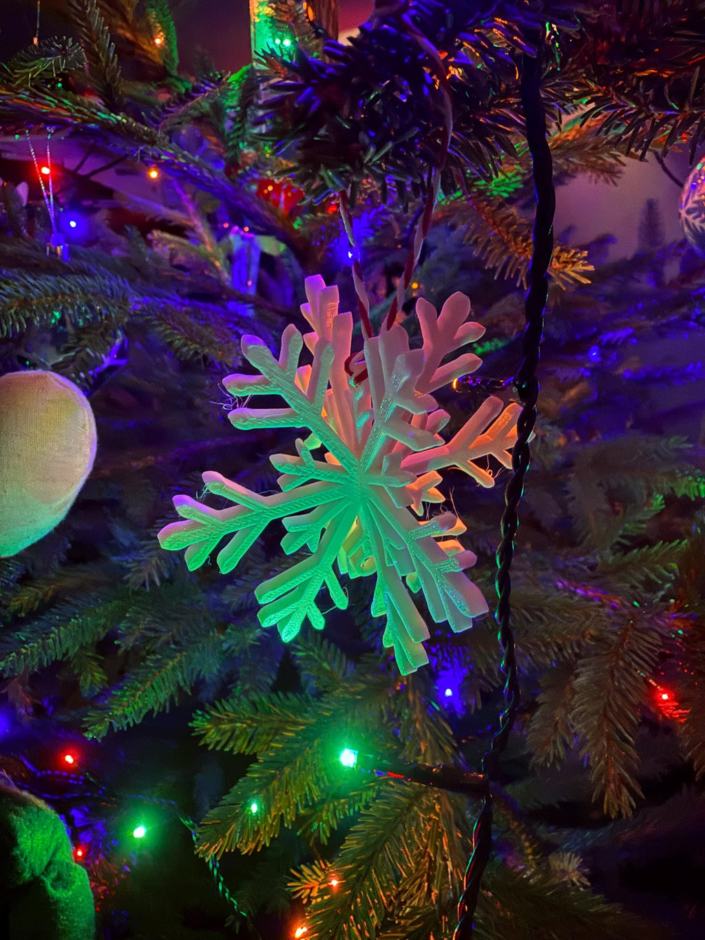 Decorative snowflake ornament on a Christmas tree with colorful lights