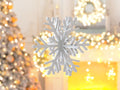 White snowflake ornament with festive lights and decorations in the background