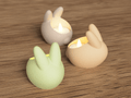 Three rabbit-shaped candle holders with lit candles on a wooden surface