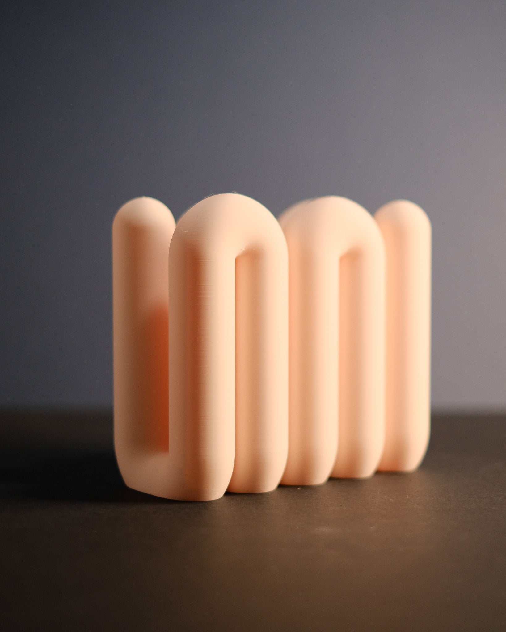 Row of beige ceramic sculptures on a dark surface with a gray background