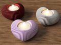 Three ribbed candle holders in red, purple, and gray with lit candles on a wooden surface.