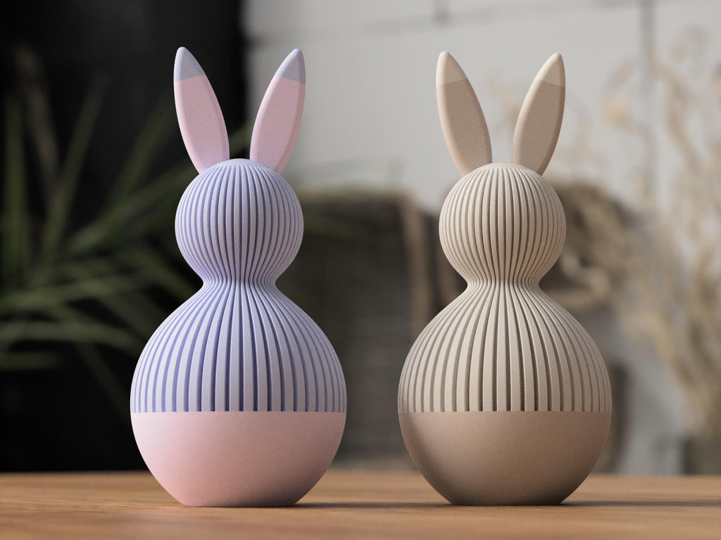 Two rabbit-shaped lamps, one purple and one beige, on a wooden surface with a blurred indoor background.