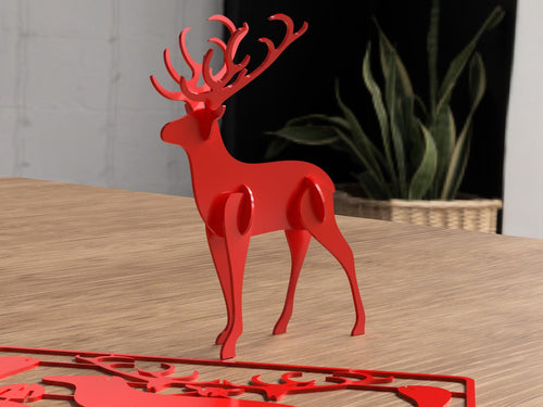 Red deer-shaped decorative item on a wooden surface with a plant in the background.