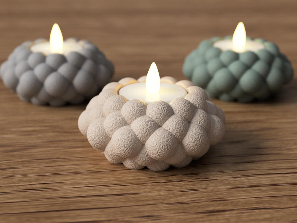 Three textured candle holders with lit candles on a wooden surface
