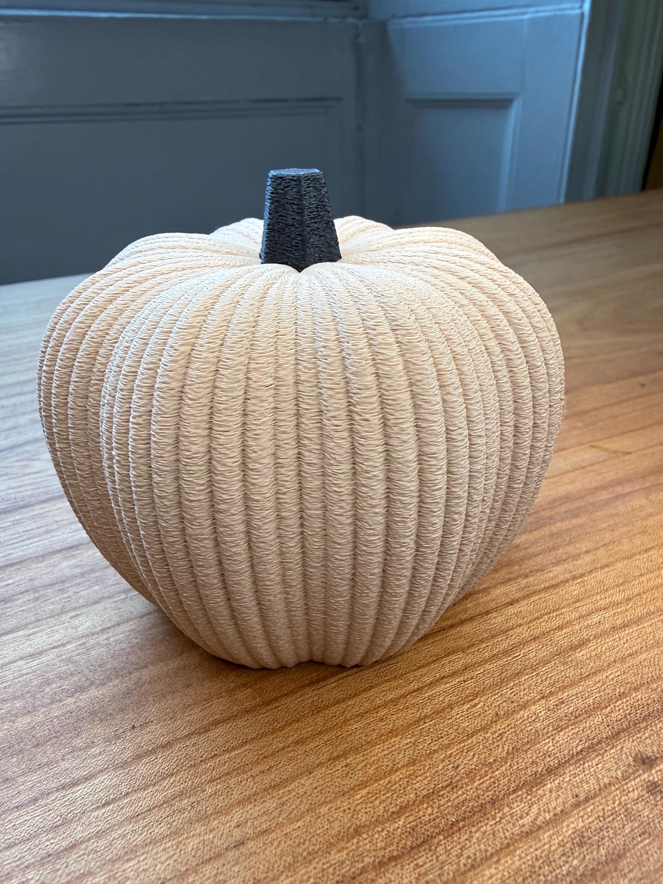 Decorative pumpkin made of beige yarn on a wooden surface with a blue wall in the background