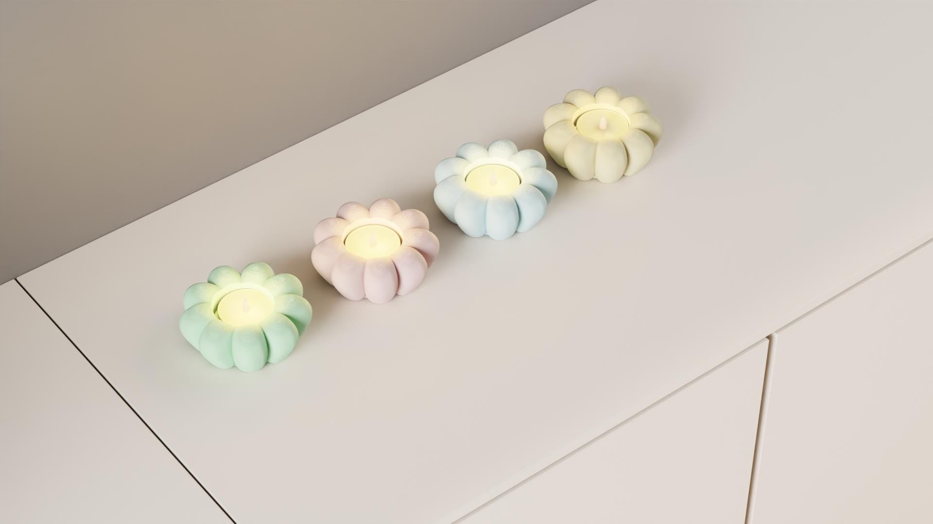 Four pastel-colored flower-shaped candles on a white surface.