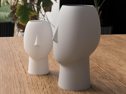 Two white ceramic vases on a wooden surface with blurred greenery in the background