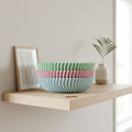 Stack of colorful ceramic bowls on a wooden shelf with a plant and framed picture in the background.